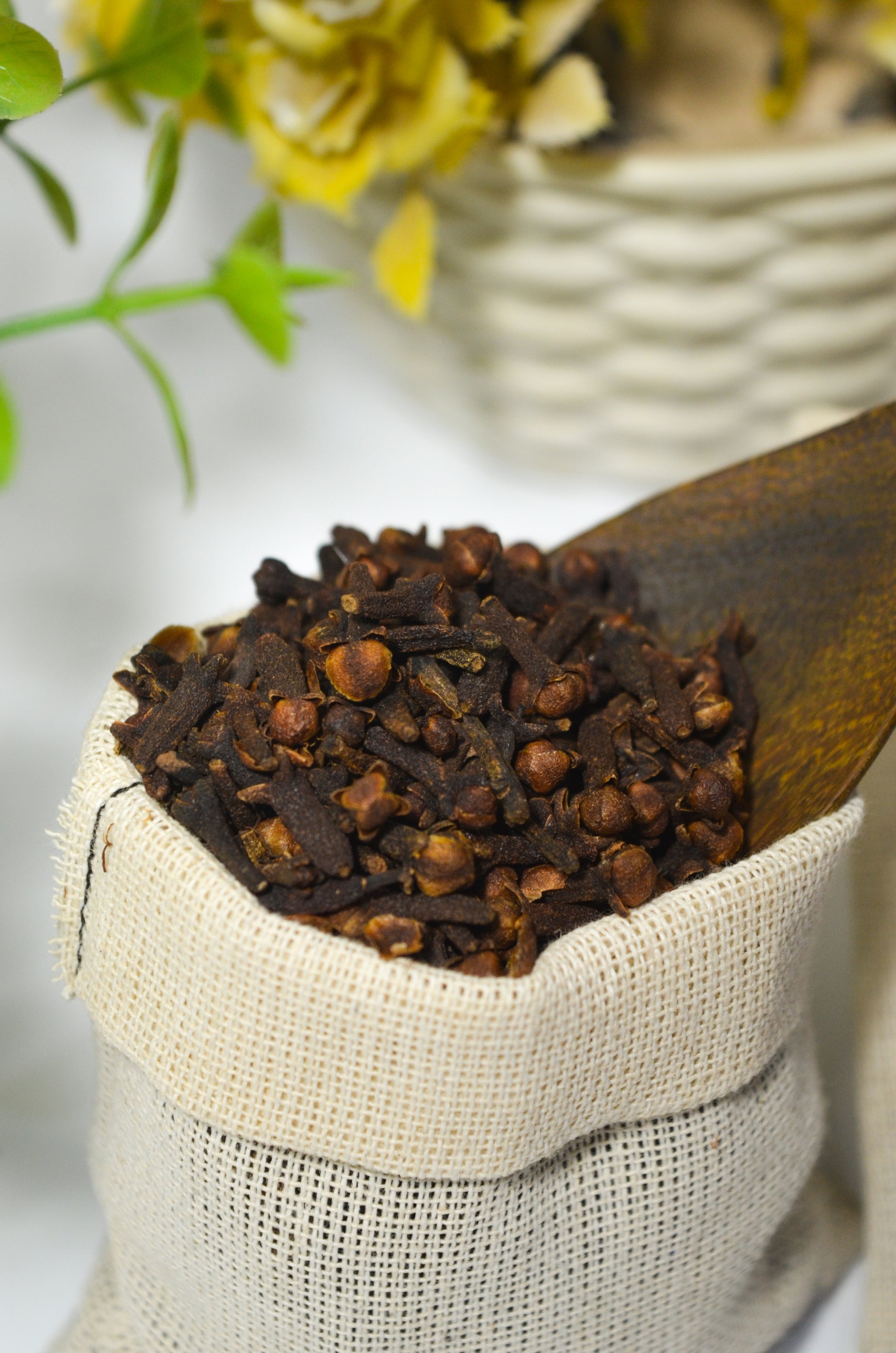 Wooden scoop filled with cloves in a white sack with a blurred floral background