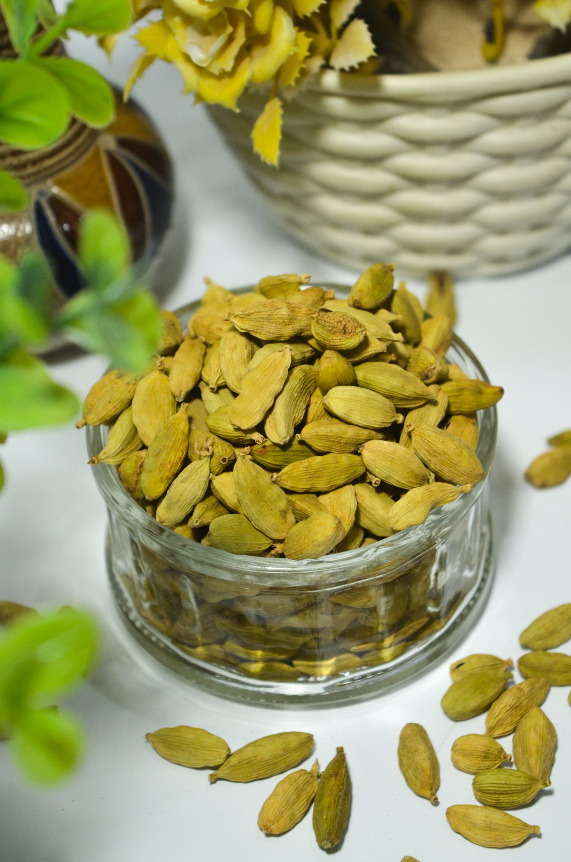 Glass jar filled with cardamom pods on a white surface with greenery.