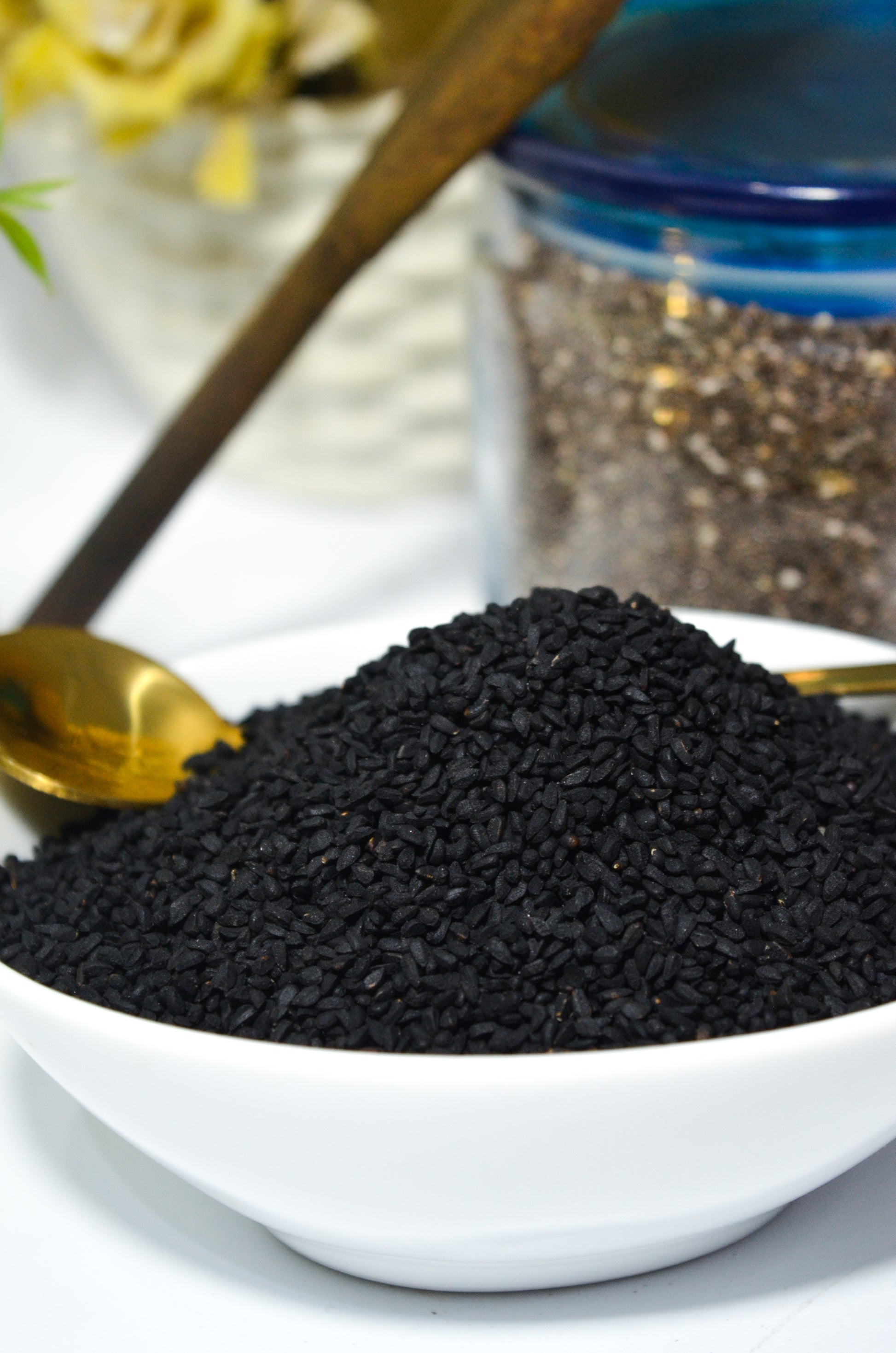 Black seeds in a white bowl with a gold spoon, blurred background
