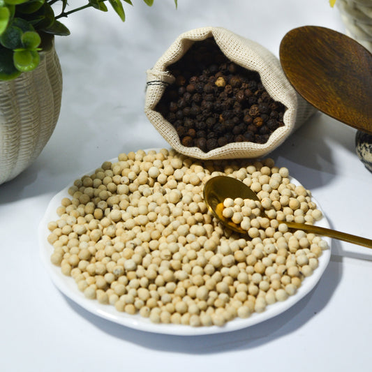 White plate with White Pepper, a bronze spoon, and a plant on a light background.